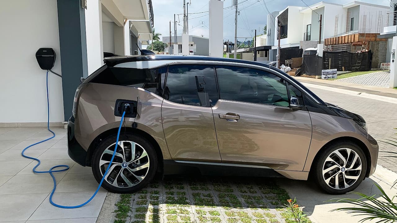 Bronze BMW i3 electric car charging with blue cable at home charging station in residential driveway