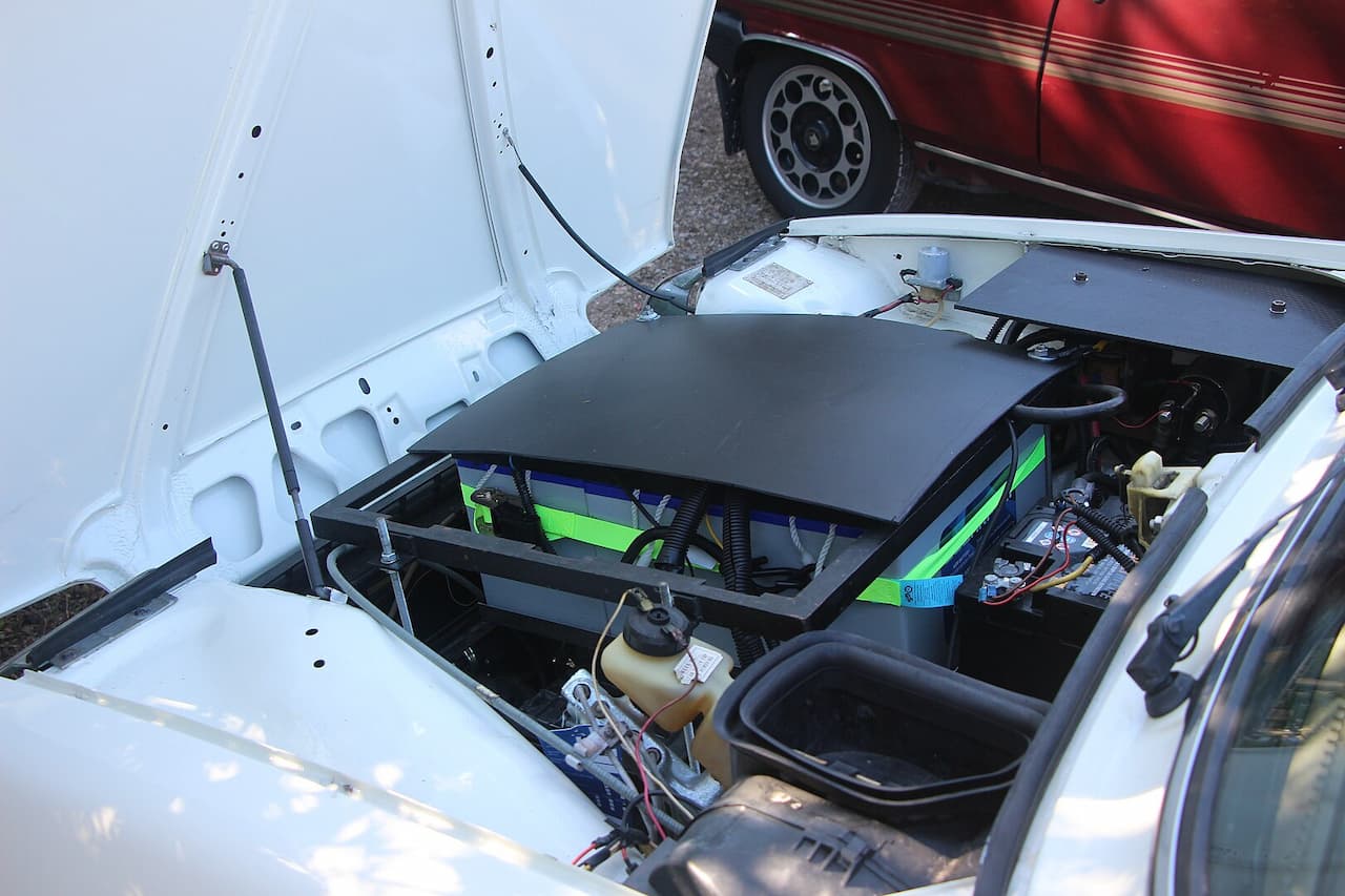 White Renault 5 with open hood showing six green batteries installed in engine bay for electric conversion