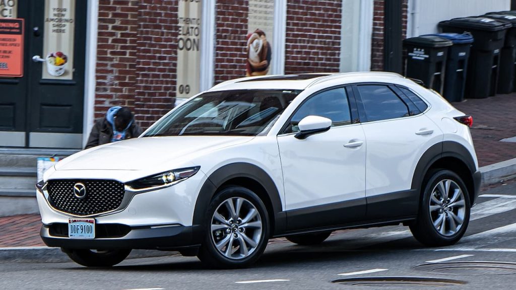 White 2025 Mazda CX-30 SUV with black wheel arches parked on brick-paved street near storefronts