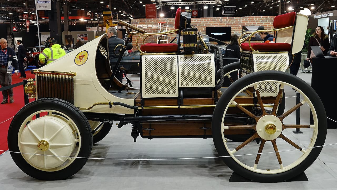 Historic Semper Vivus early automobile with white body, wooden spoked wheels displayed at indoor car exhibition