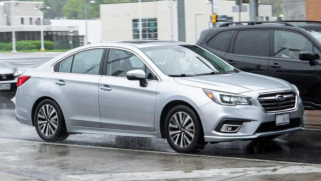 Silver 2025 Subaru Legacy driving on wet road with LED headlights and multi-spoke alloy wheels