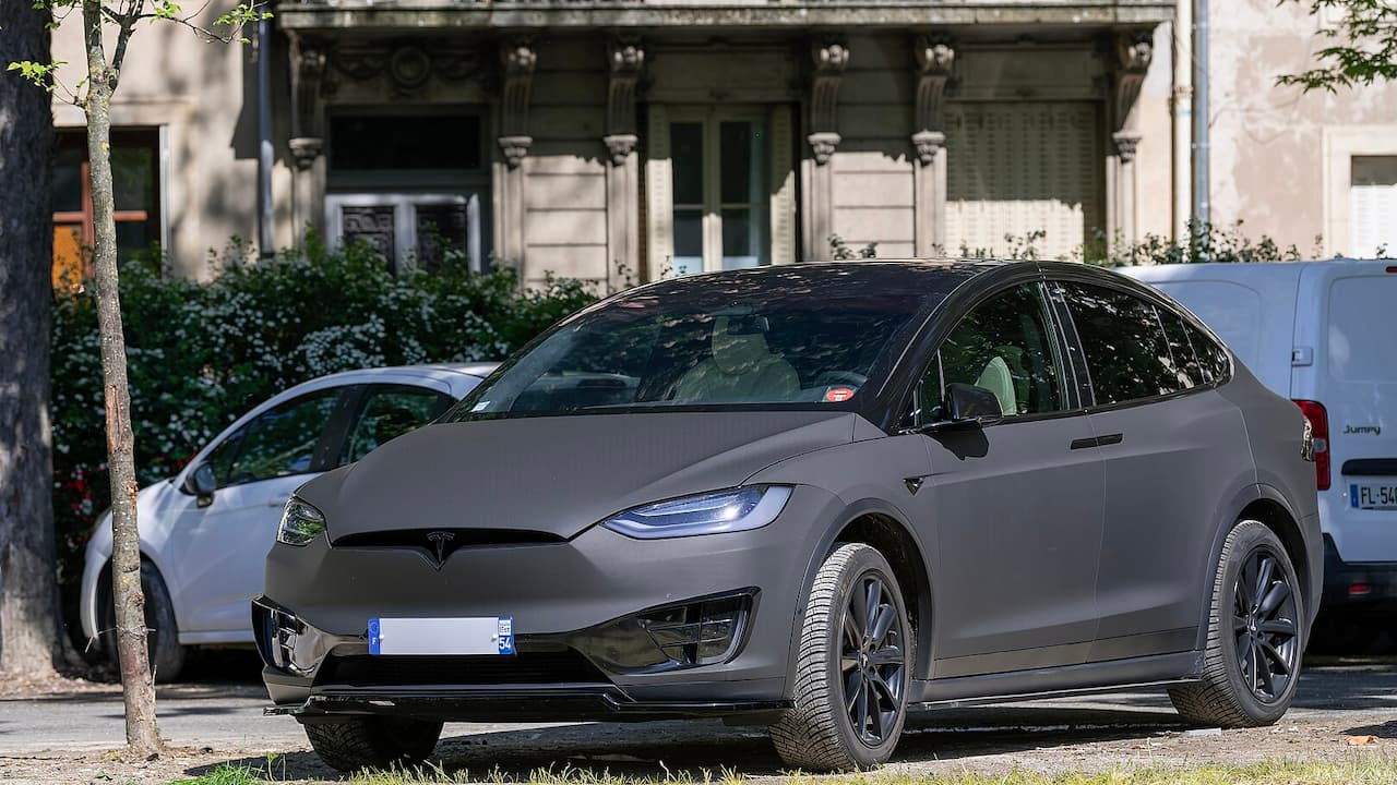 Gray 2025 Tesla Model X electric SUV parked on street with distinctive falcon-wing doors, modern LED headlights, and sleek aerodynamic design