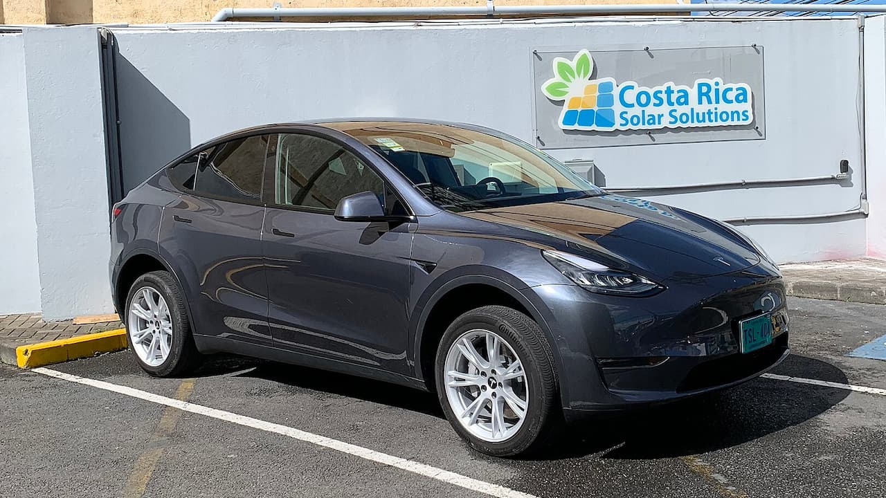 Dark gray 2021 Tesla Model Y parked in parking space next to white building with Costa Rica Solar Solutions sign