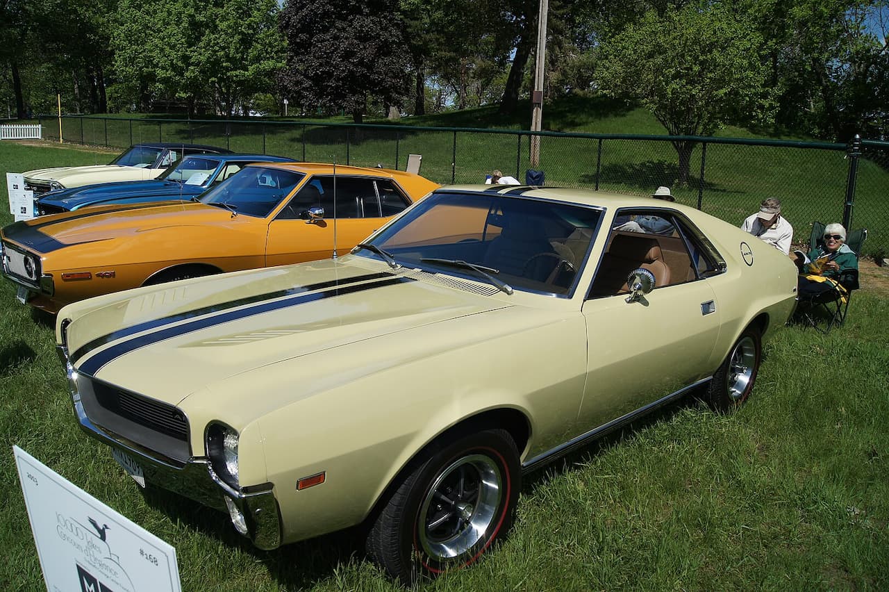 Classic 1969 AMC AMX muscle car with cream paint and blue racing stripes displayed at outdoor car show