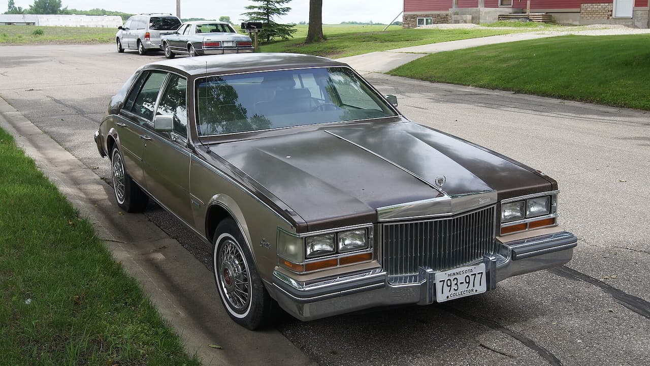 Bronze 1981 Cadillac Seville Bustleback parked on residential street with wire wheels, chrome grille, and Minnesota license plate