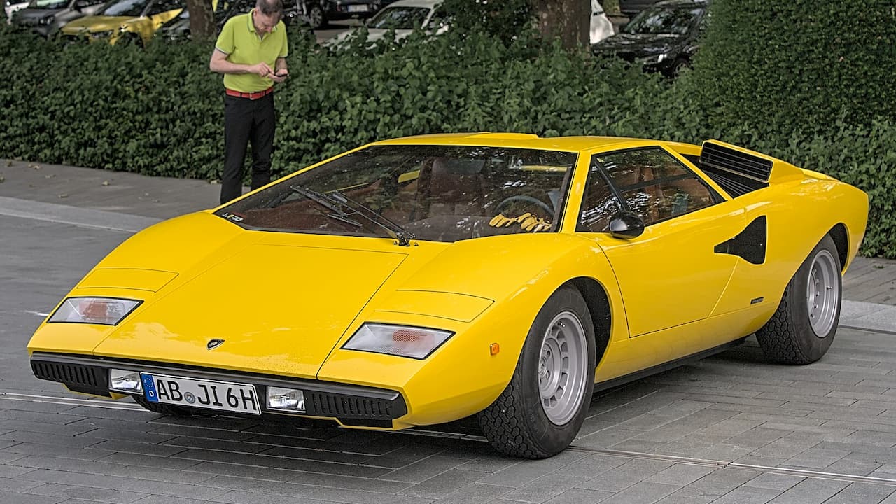 Yellow Lamborghini Countach LP400 with distinctive wedge design parked on stone pavement with person in background