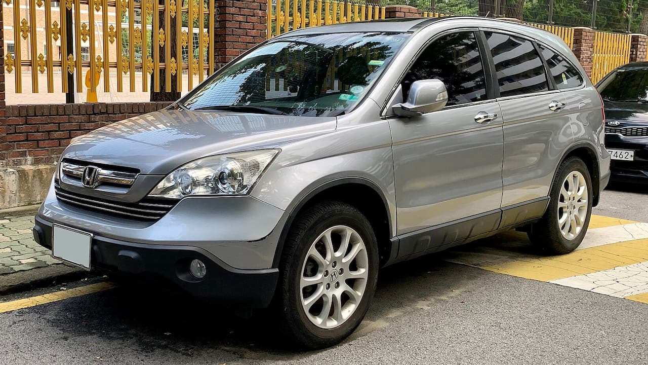 Silver 2022 Honda CR-V parked on street beside brick wall with decorative golden metal fence and paved sidewalk