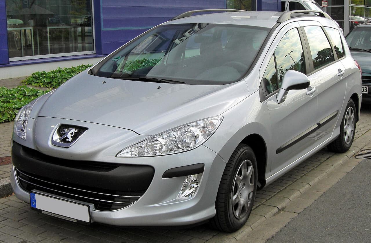 Silver Peugeot 308 SW parked on cobblestone street with distinctive lion badge and panoramic sunroof visible
