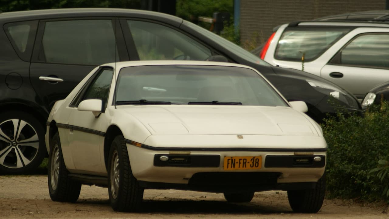 White 1984 Pontiac Fiero mid-engine sports car with European license plate parked among other vehicles outdoors
