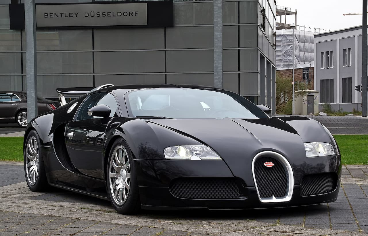 Black Bugatti Veyron with distinctive horseshoe grille parked on cobblestones outside Bentley Düsseldorf dealership building