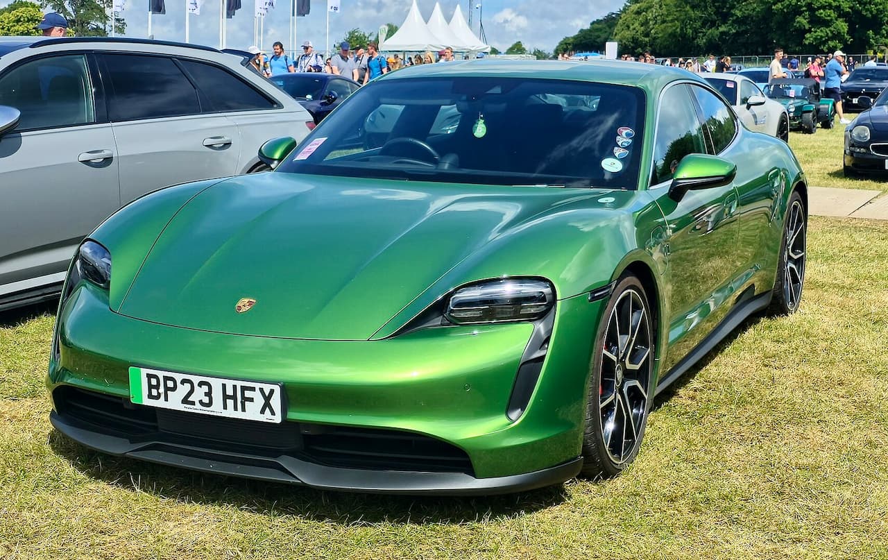 Metallic green Porsche Taycan electric sports car with UK license plate parked on grass at outdoor car show event
