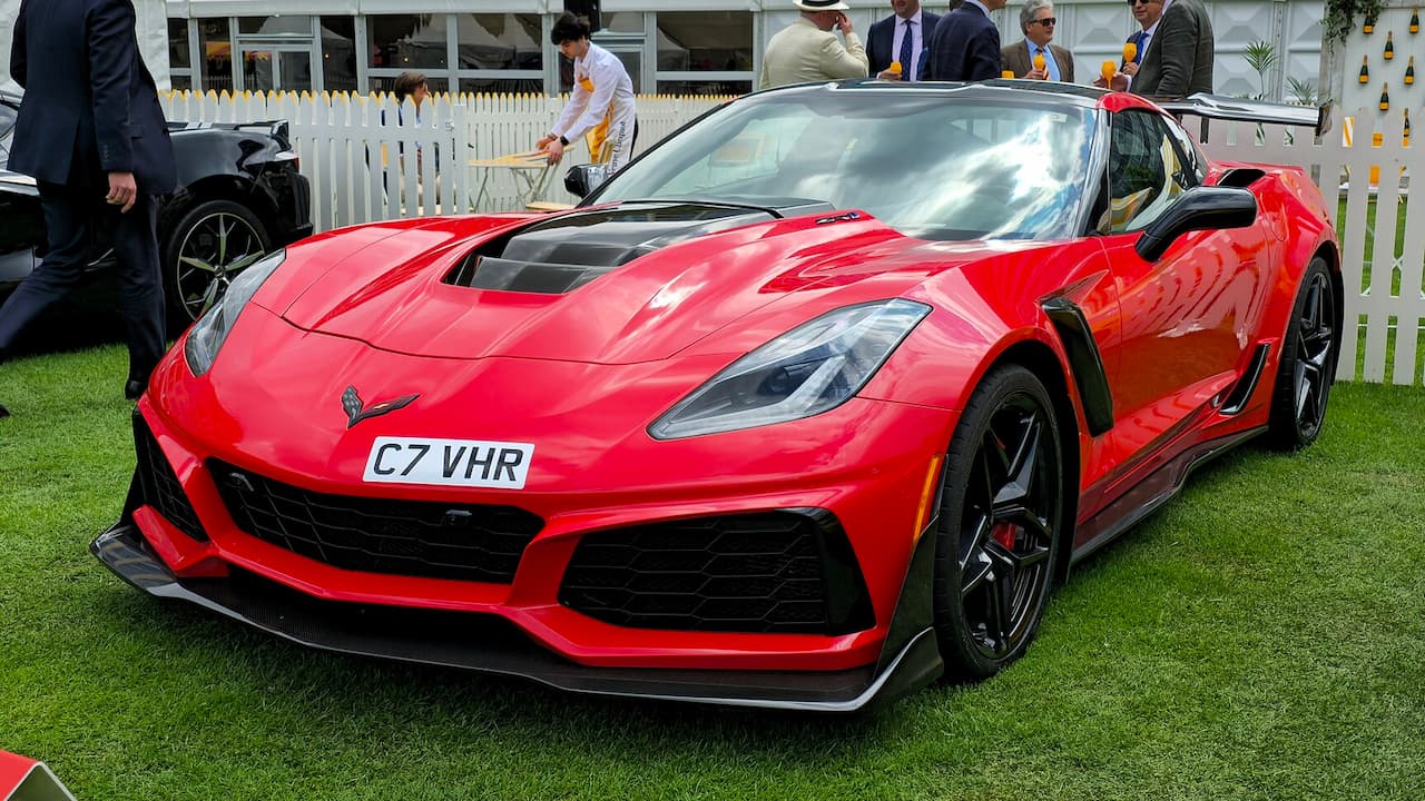 Red Chevrolet Corvette C7 sports car with black aerodynamic elements displayed on grass at outdoor car show