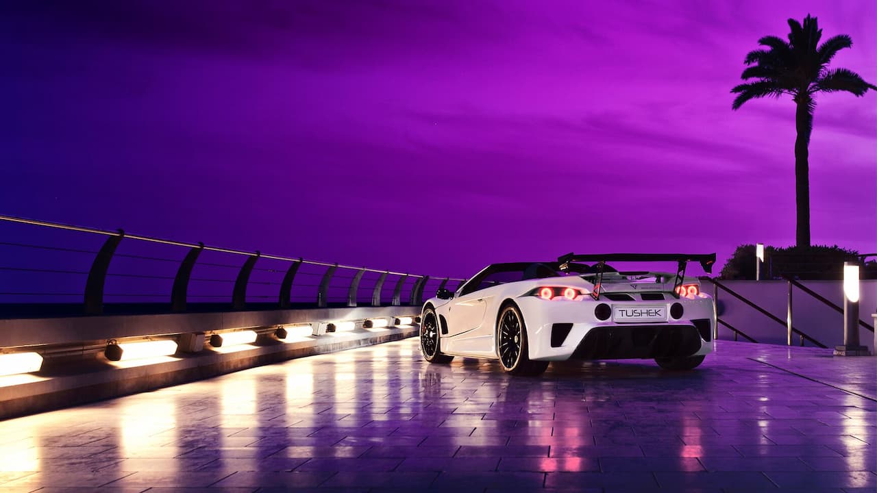 White Tushek Renovatio T500 supercar with large rear wing parked on wet pavement against purple twilight sky