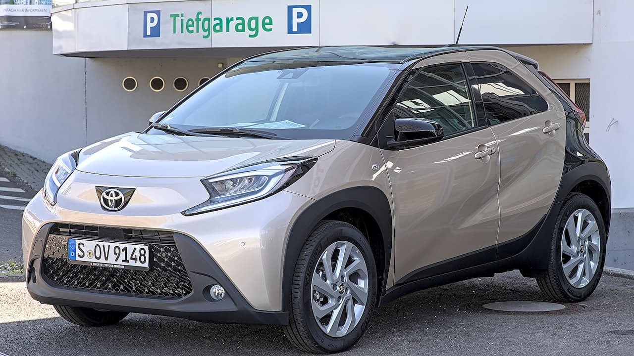 Beige Toyota Aygo X compact crossover parked outside Tiefgarage underground parking entrance with German license plate and distinctive Toyota styling