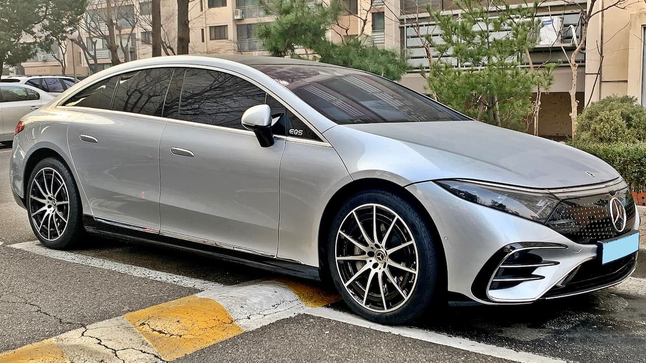 Silver Mercedes-Benz EQS with sleek aerodynamic design and multi-spoke wheels parked in urban setting