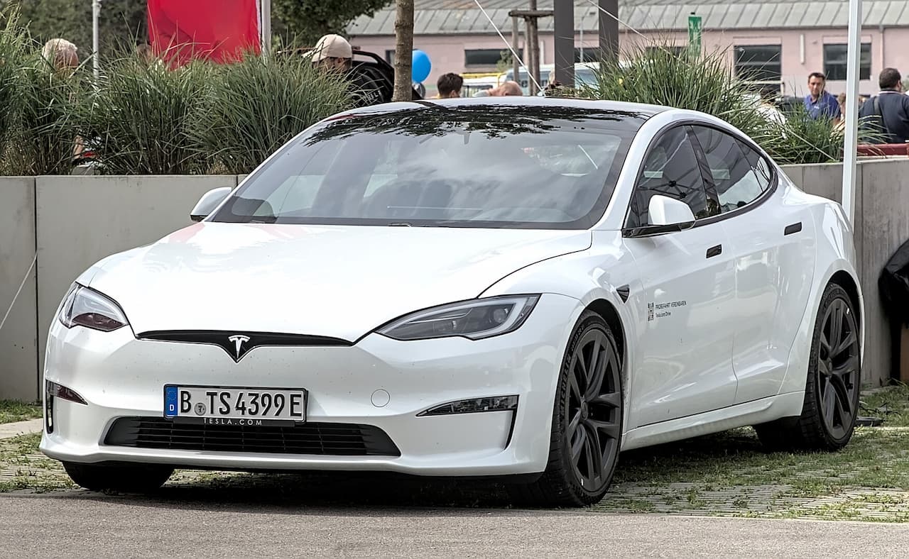 White Tesla Model S electric vehicle with sleek design, black roof, distinctive headlights, and German license plate parked outdoors
