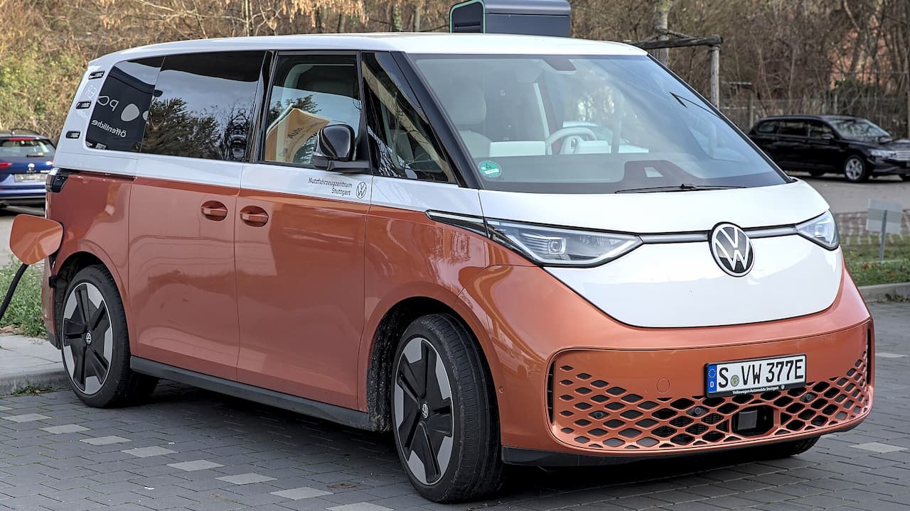 Orange and white Volkswagen ID.Buzz electric van parked on cobblestone street with charging cable connected and German license plate