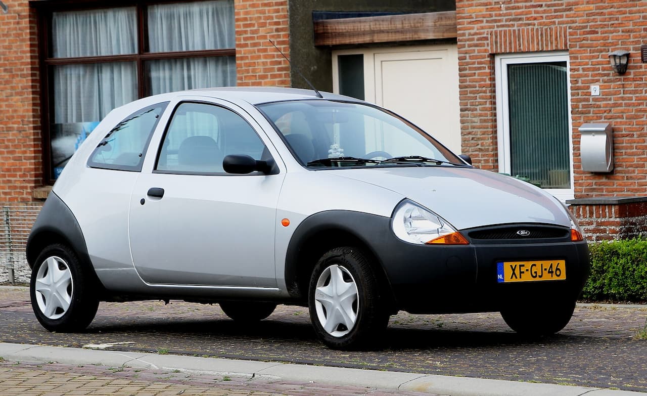 Silver Ford Ka with black plastic wheel arches and Dutch license plate parked on cobblestone street near brick houses
