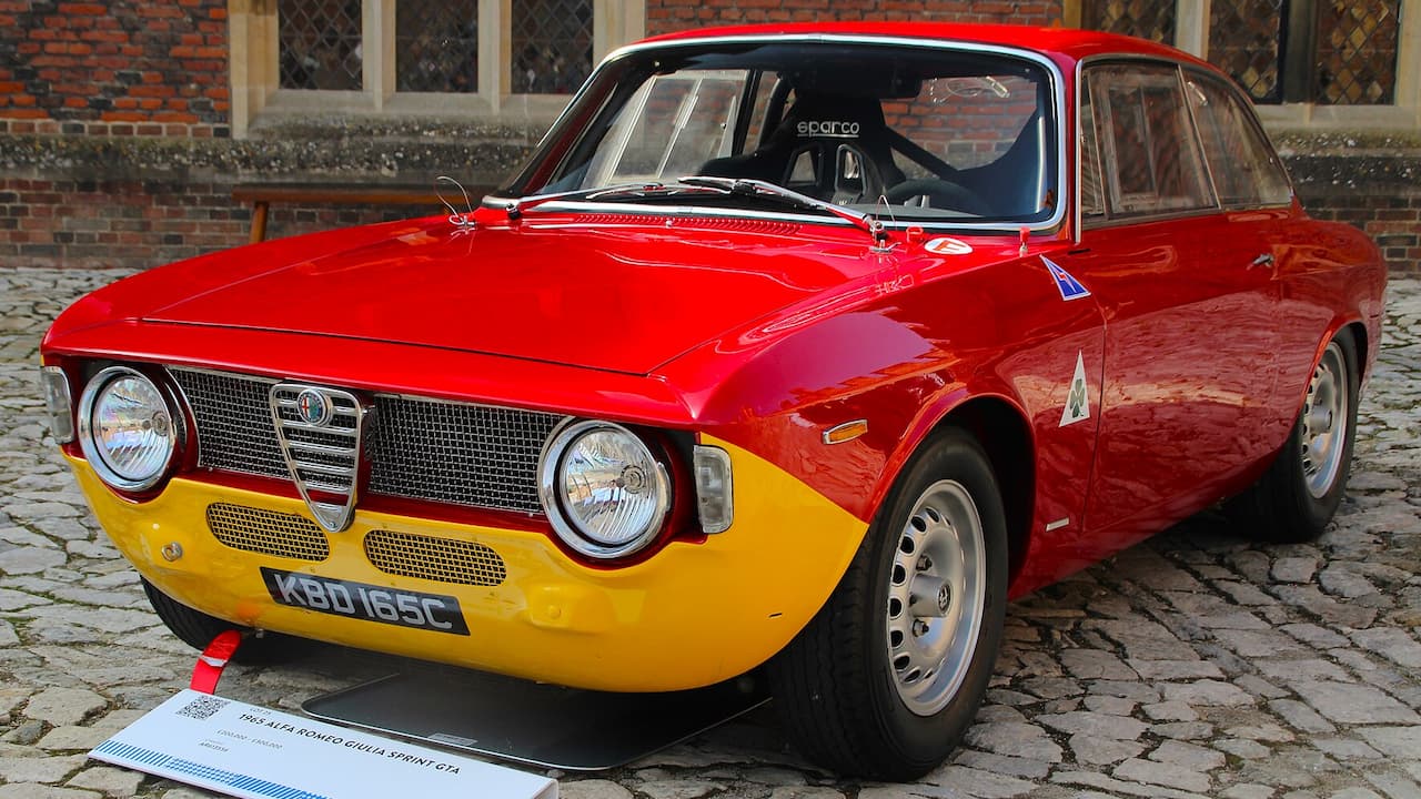 Red and yellow Alfa Romeo Giulia Sprint GTA with UK license plate parked on cobblestones