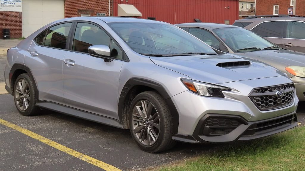 Silver Subaru WRX sedan parked in parking lot with hood scoop and sporty body cladding visible