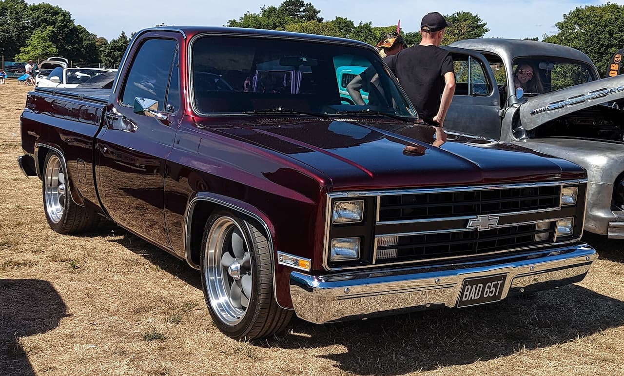 Dark burgundy 1985 Chevy C/K pickup truck with lowered stance and custom wheels at outdoor car show event