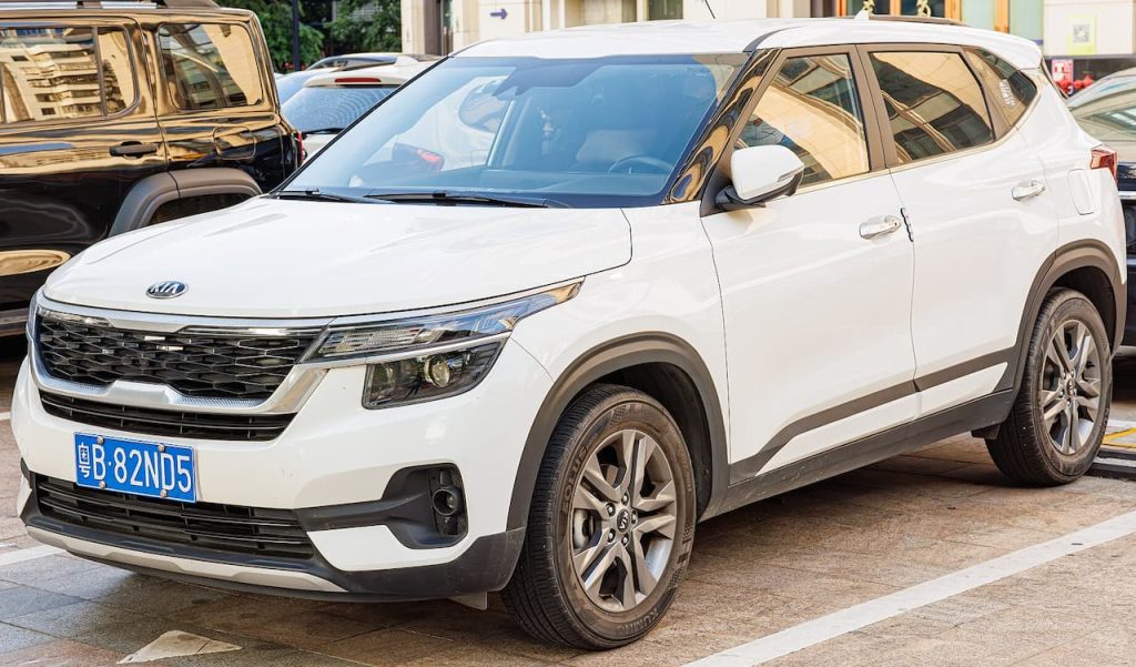 White 2025 Kia Seltos SUV with blue Chinese license plate parked on street among other vehicles