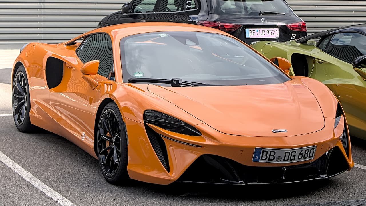 Orange McLaren Artura with black wheels and carbon fiber accents parked in lot with other vehicles