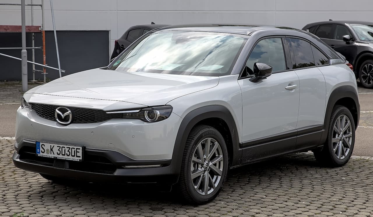Silver Mazda MX-30 electric SUV parked on cobblestone surface with European license plate and distinctive modern crossover design
