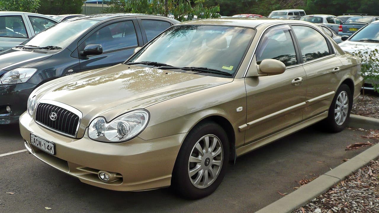 Gold 2003 Hyundai Sonata parked in parking lot with alloy wheels and distinctive oval headlights among other vehicles