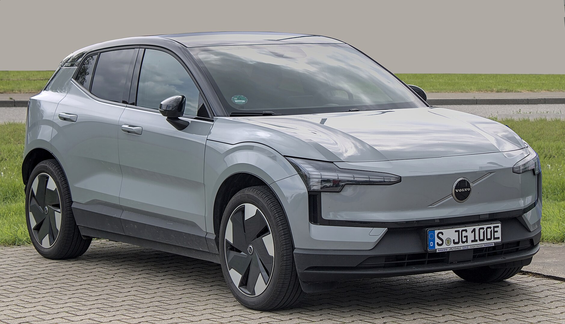 Silver Volvo EX30 Recharge electric SUV with distinctive headlights and aerodynamic wheels parked on cobblestone surface