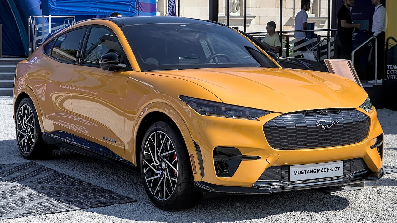 Orange Ford Mustang Mach-E GT electric SUV with sporty styling displayed at automotive event with crowds