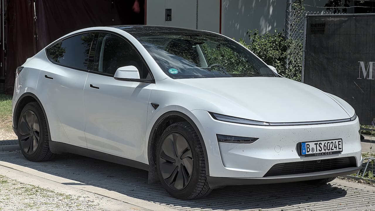 White 2025 Tesla Model Y electric vehicle with dark aerodynamic wheels parked on brick pavement near modern buildings