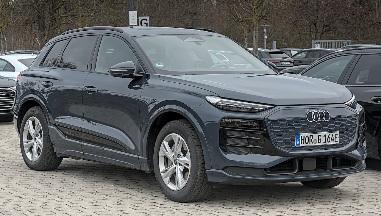 Dark gray Audi Q6 e-tron electric SUV parked in parking lot with distinctive LED headlights and honeycomb grille design