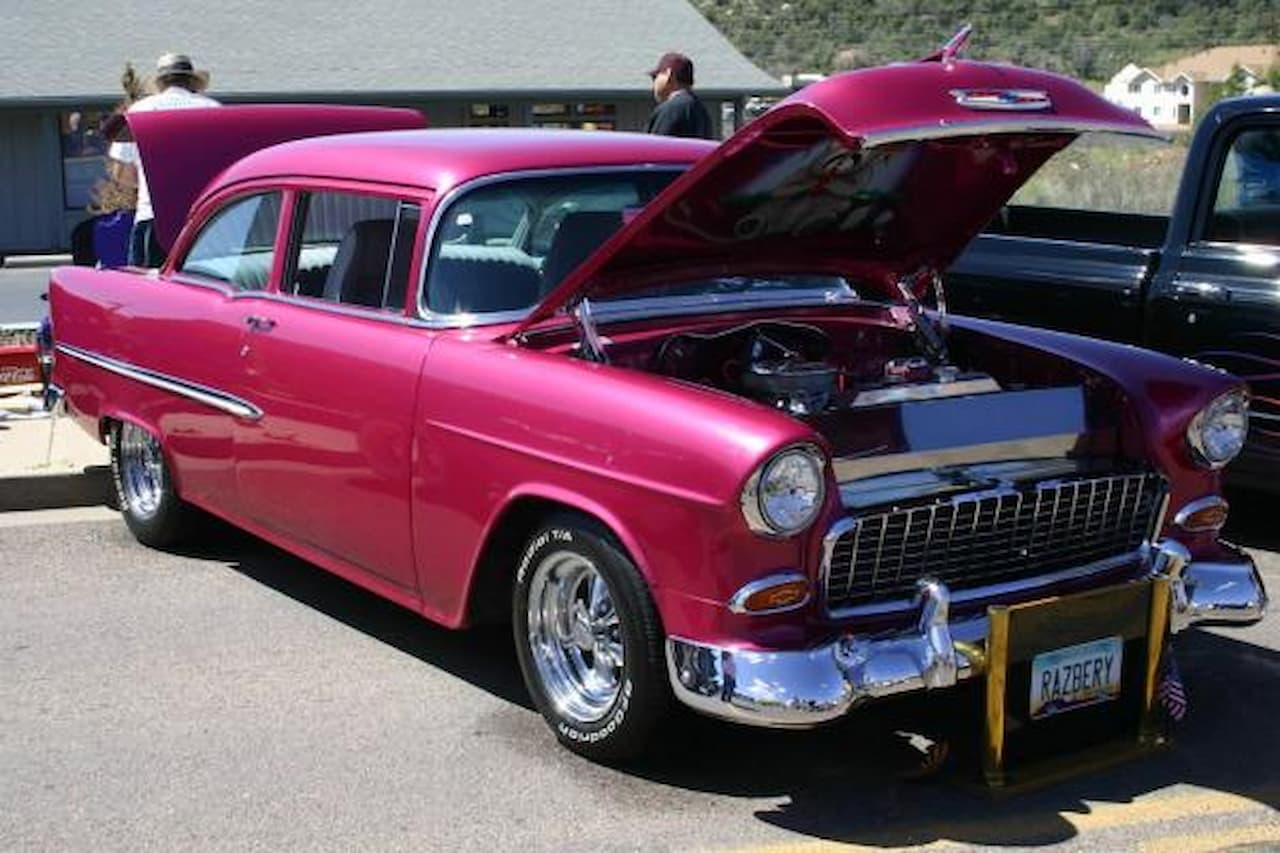 1955 Chevrolet 150 sedan with open hood displaying engine at car show with chrome wheels and bumpers