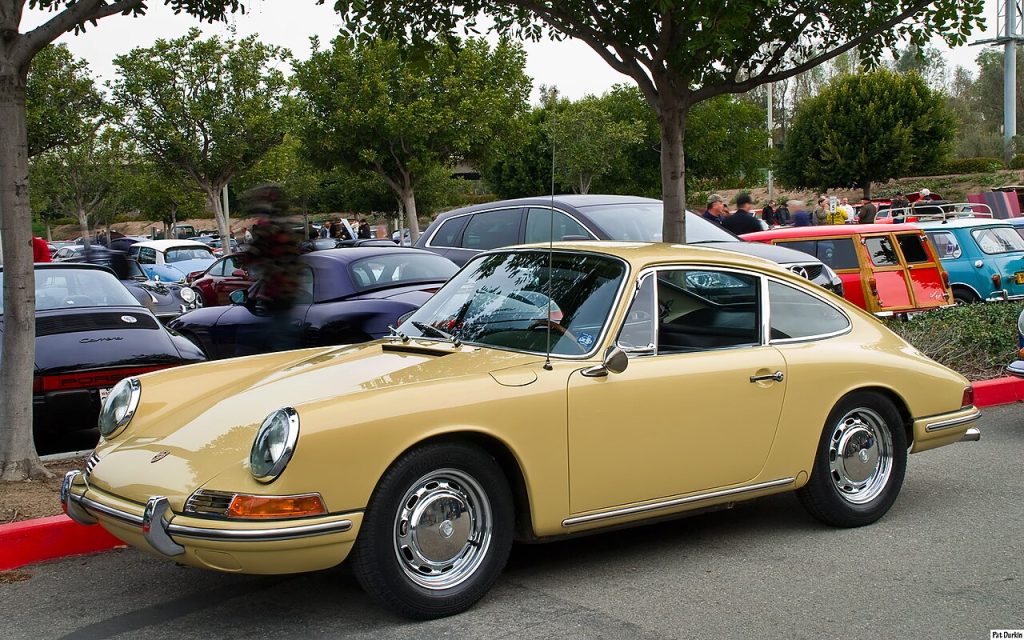 Yellow 1964 Porsche 911 with chrome bumpers and classic wheels parked at outdoor car show with other vintage vehicles