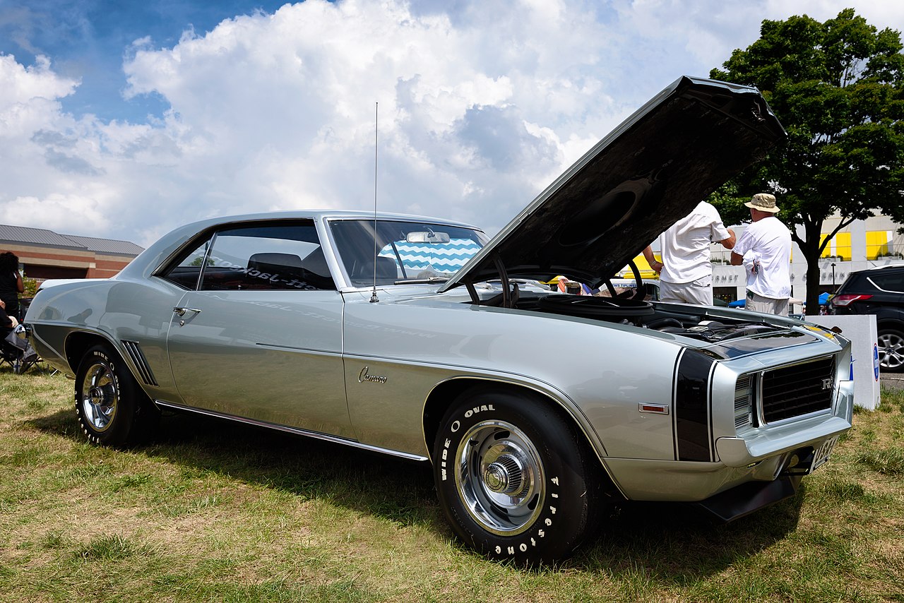 Silver 1969 Chevrolet Camaro ZL1 with hood open displaying engine at outdoor car show under cloudy sky