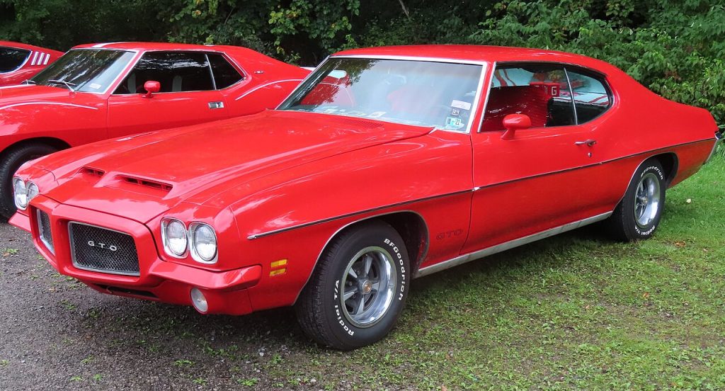 Red 1971 Pontiac GTO muscle car parked on grass with chrome bumpers, dual headlights, and classic sporty coupe styling