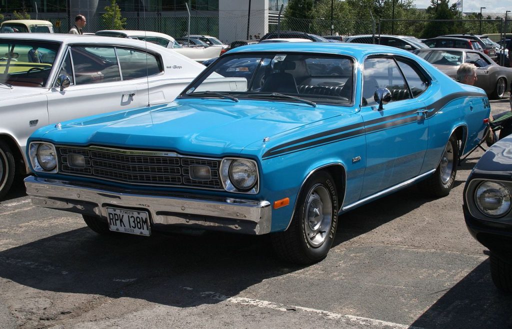 Blue 1973 Plymouth Duster classic muscle car with black racing stripes parked in sunny lot