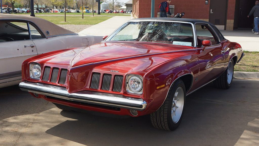 Red 1973 Pontiac Grand Am muscle car with distinctive split grille and wide tires parked on pavement
