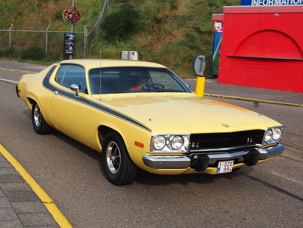 Yellow 1974 Plymouth Road Runner classic muscle car with black stripes parked on street pavement