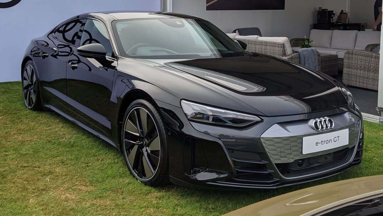 Black Audi e-tron GT electric vehicle with aggressive styling and large wheels displayed on grass at auto show