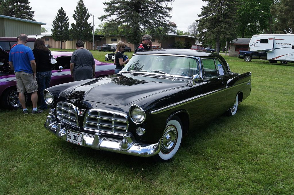 Black 1956 Chrysler 300B with chrome grille and whitewall tires parked on grass at classic car show event