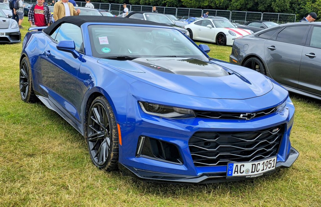Blue 2024 Chevrolet Camaro ZL1 sports car parked on grass at car show with other vehicles in background