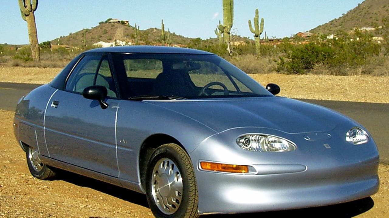 Silver 1996 GM EV1 electric car parked on desert road with saguaro cacti and mountains in Arizona landscape