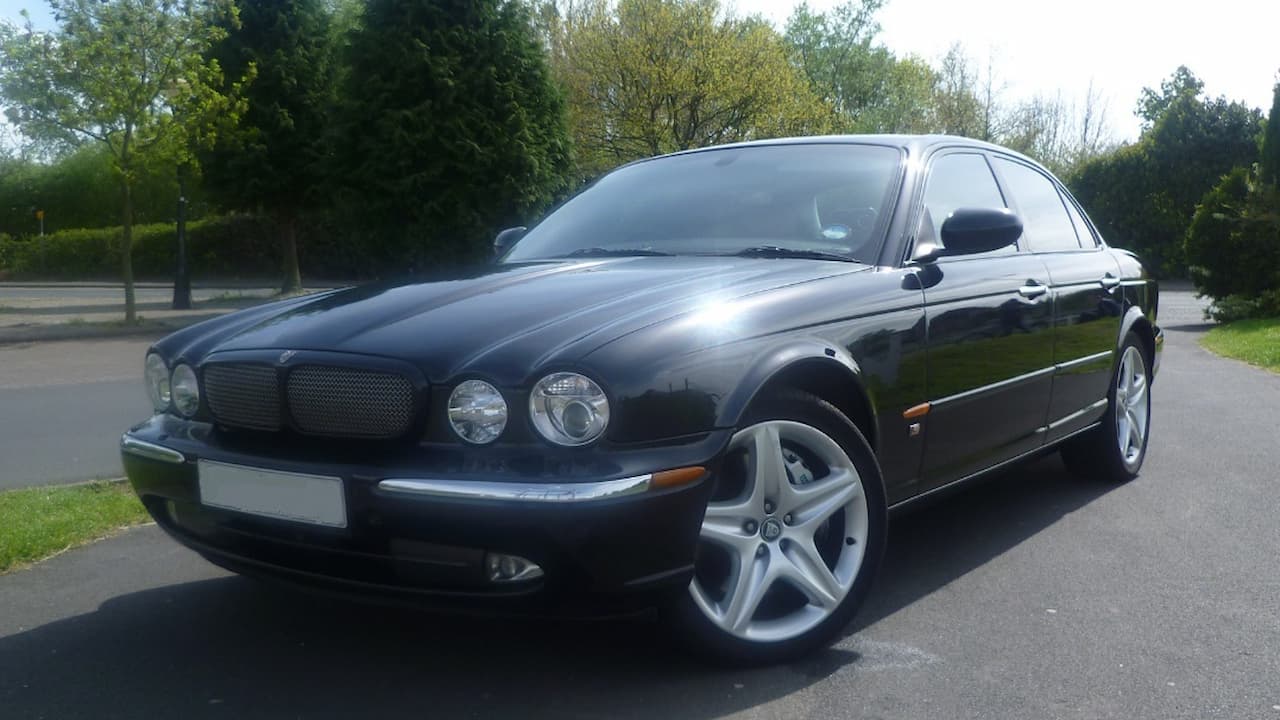 Black Jaguar X350 sedan parked on asphalt road with trees and grass in background on sunny day