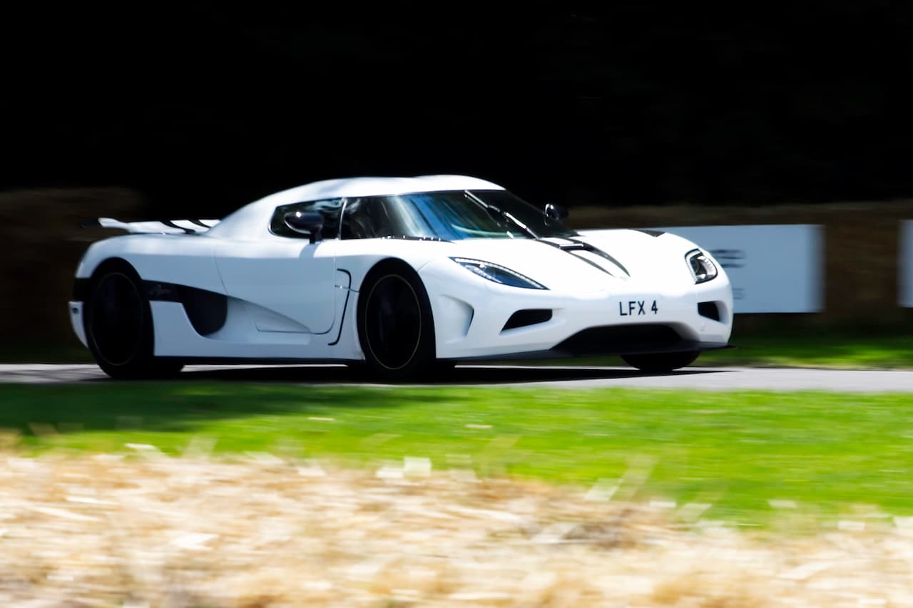 White Koenigsegg Agera R hypercar with large rear wing and license plate "LFX 4" driving on track with motion blur