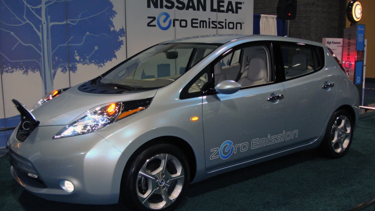 Silver 2010 Nissan Leaf electric car displayed at auto show with "Zero Emission" branding and charging station nearby