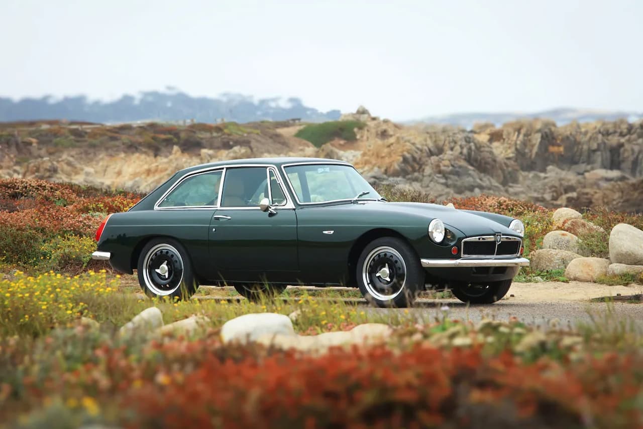 Dark green RBW Roadster Electric Sports Car with chrome details parked in rugged coastal landscape with rocks and wildflowers