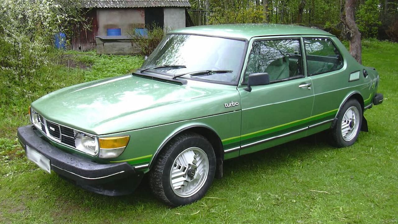 Green Saab 99 Turbo classic car parked on grass with rural building and trees in background