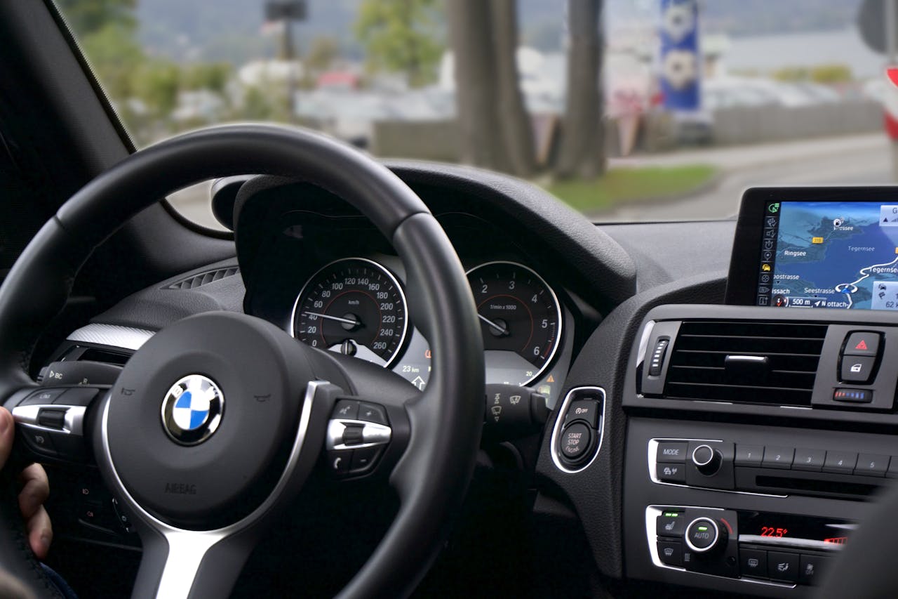 Interior view of BMW car showing steering wheel, dashboard, speedometer, navigation screen, and climate controls from driver's perspective